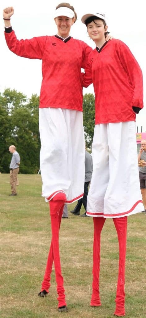 2 women on stilts having a kick-about with a football