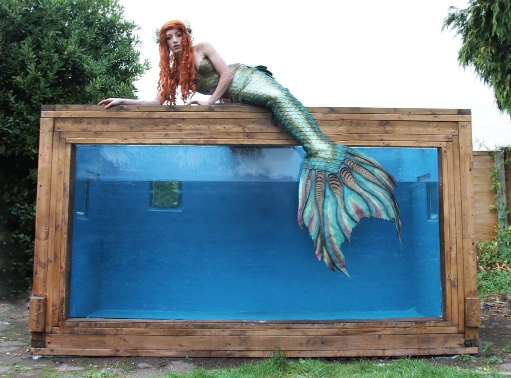 Character dressed as a mermaid lying on the top of a wooden frame