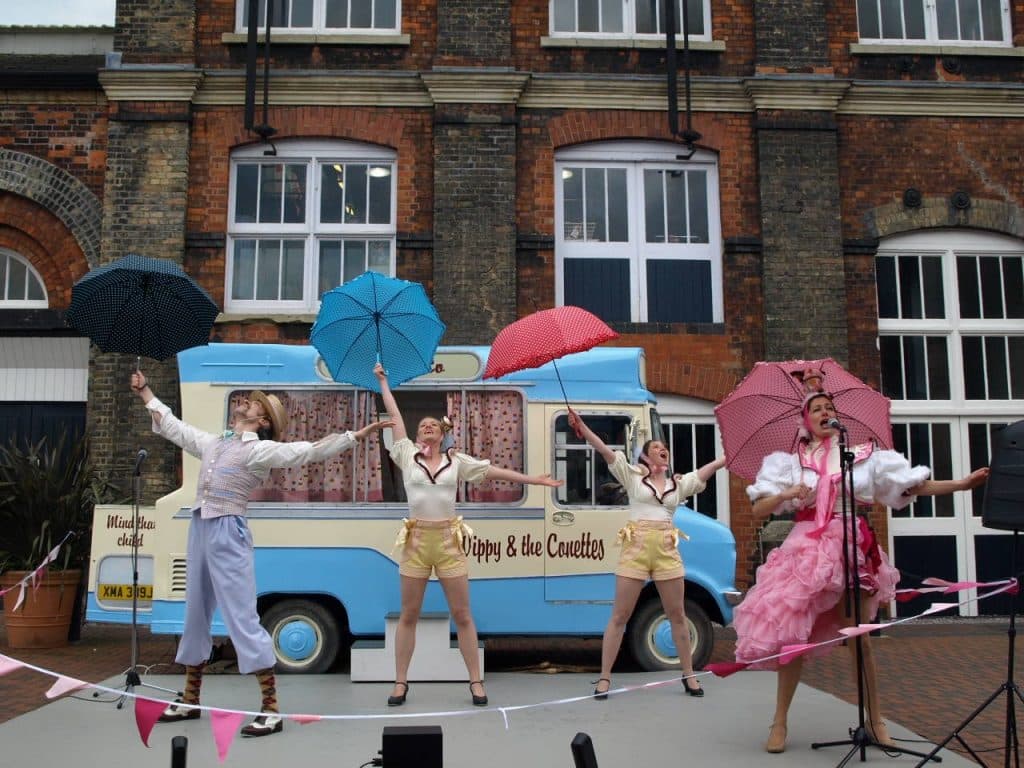 Characters dressed in 1950’s outfits dancing with umbrellas in front of a Mr Wippy ice cream van